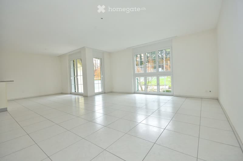 Empty room with white tiled flooring, large windows, and white walls. No furniture or equipment present.