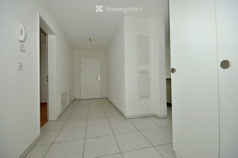 Empty hallway with white walls, tiled floor, and several doors leading to other rooms.