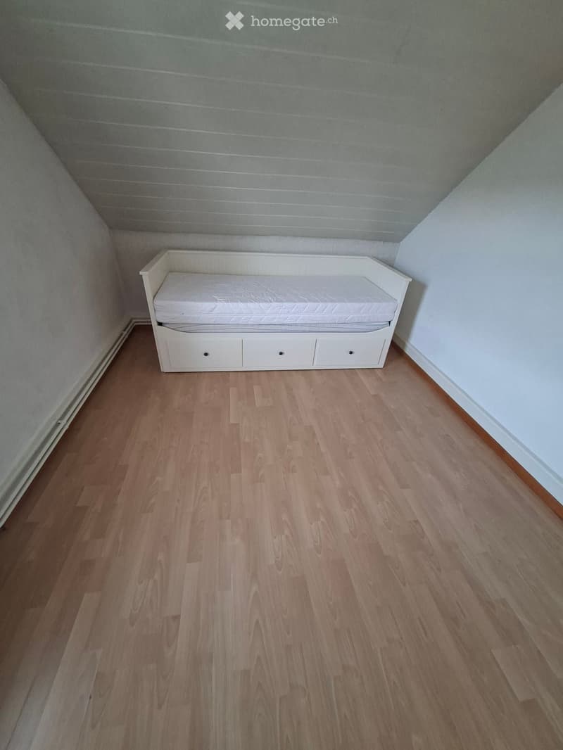 A small, furnished room with a single sofa and wooden flooring.