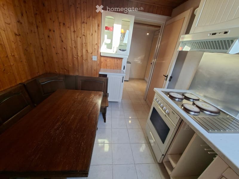 A cozy kitchen and dining area with wooden walls, a wooden dining table, chairs, and modern appliances including an oven and refrigerator.