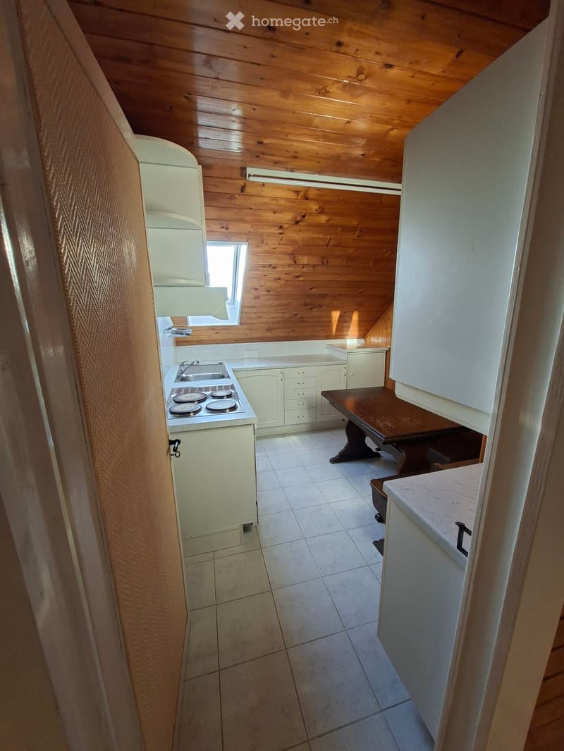 Compact kitchen with white cabinets, a small wooden table, a stove, and a sink, featuring wooden walls and a tiled floor.