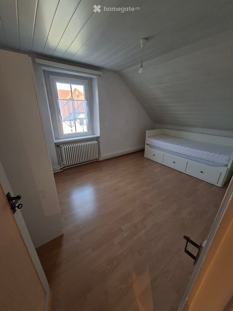Bright attic bedroom with wooden flooring, a single bed with drawers, a window with a view, and a radiator.