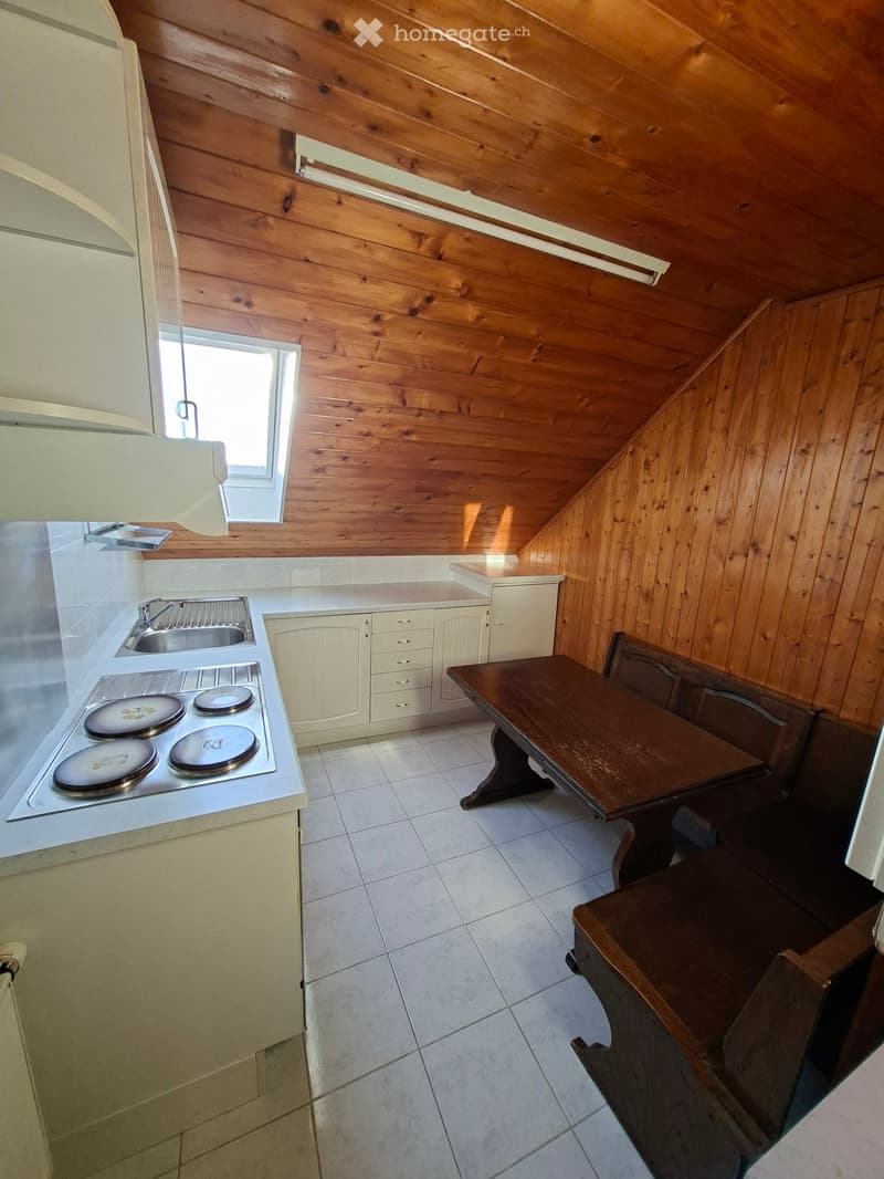 Cozy kitchen with wooden walls and ceiling, featuring a stove, sink, cabinets, and a small dining table with chairs.