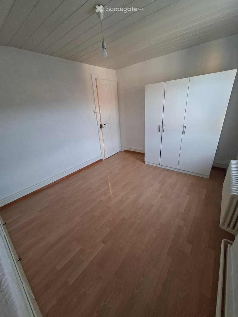 Empty room with wooden flooring, white walls, and built-in white closet units. A single door is visible on the left side.