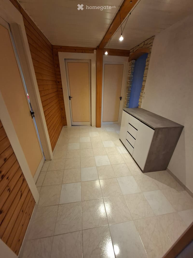 A narrow hallway with tiled flooring, wooden paneling on one side, and white cabinetry on the other. Two doors are visible, one leading to a room and the other to a closet.