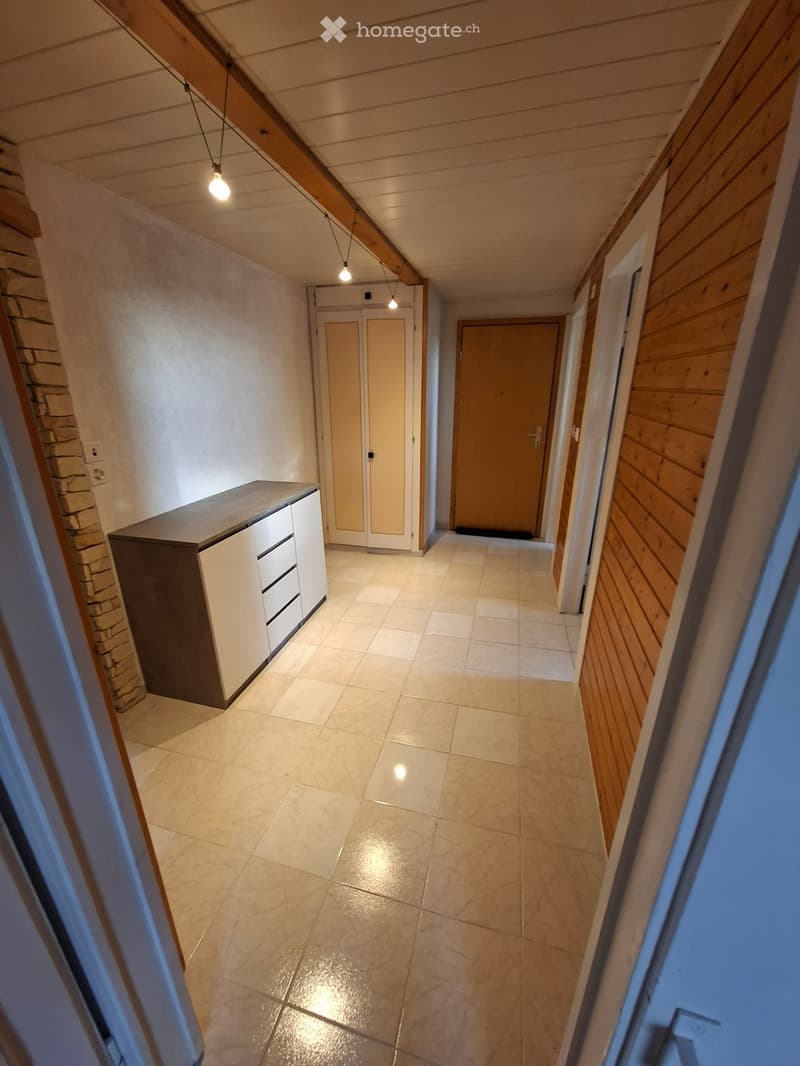 Empty hallway with tiled floor, wooden walls, and built-in storage unit on one side.