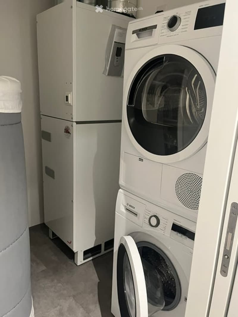 A small utility room with a refrigerator, washing machine, and dryer. The appliances are white and neatly arranged against the wall.