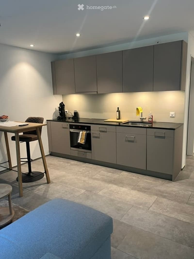 Modern kitchen with grey cabinets, a sink, an oven, and a small dining area with a table and stools.