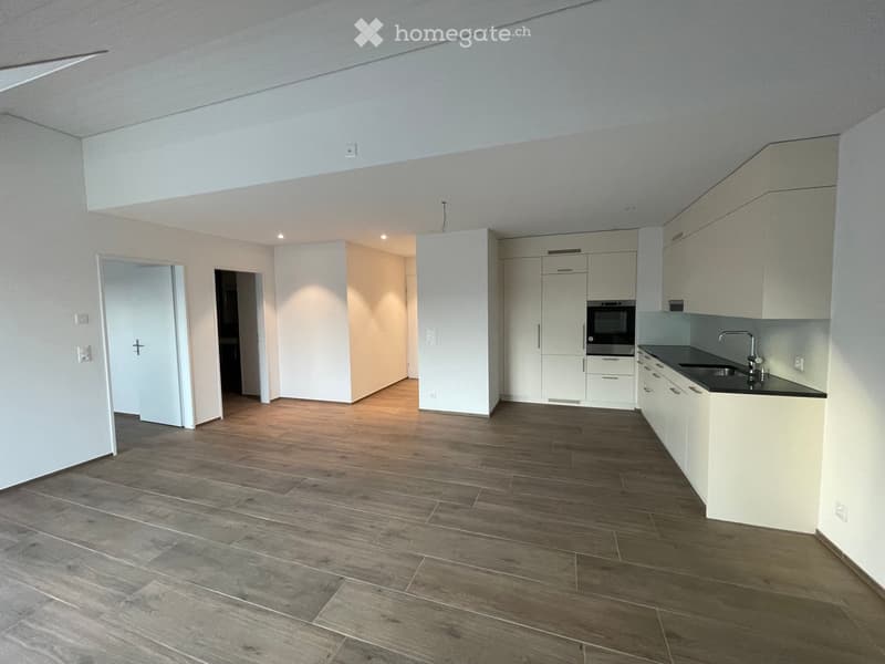 Modern kitchen with white cabinets, a black countertop, and a stainless steel sink. The floor is made of light wood planks.