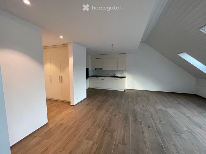 Empty room with wooden flooring, white walls, and built-in kitchen cabinets. The space includes a small kitchen area with cabinets and a sink, and the ceiling has skylight windows.