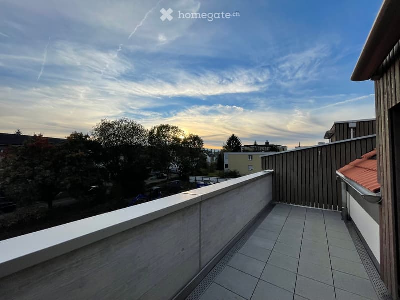 Balcony with tiled floor, white railing, and view of trees and buildings.