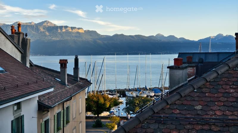 View from a rooftop showing a harbor with sailboats, a body of water, and distant mountains under a clear sky.