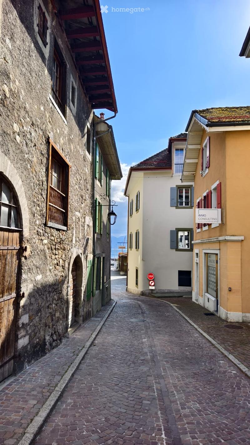 A narrow cobblestone alleyway flanked by old stone and plaster buildings with wooden shutters and small balconies.