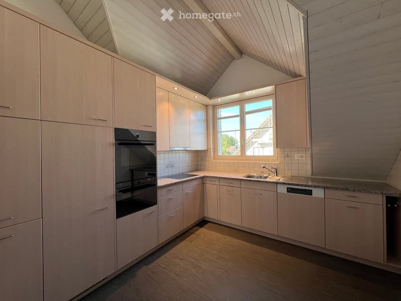 Modern kitchen with light wood cabinets, granite countertops, stainless steel appliances, and a window letting in natural light.
