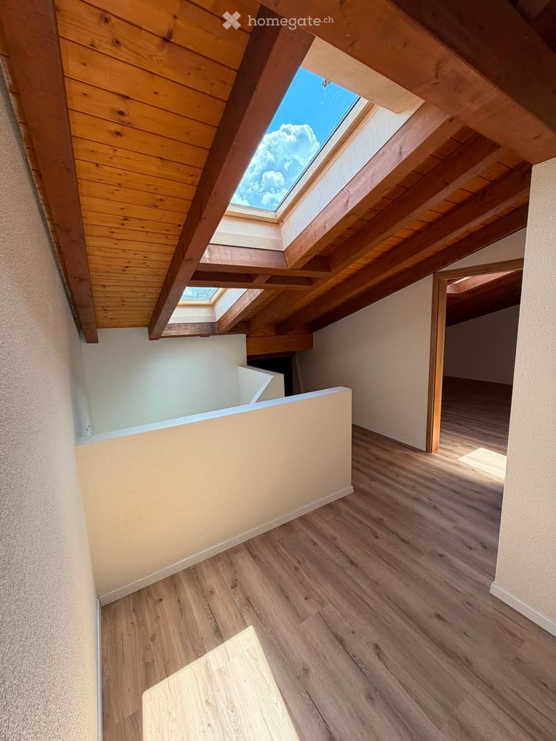 An attic space with wooden floors, exposed wooden beams, and skylight windows allowing natural light to enter.
