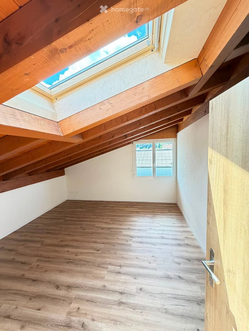 Empty attic space with wooden beams, skylight window, and wooden flooring.