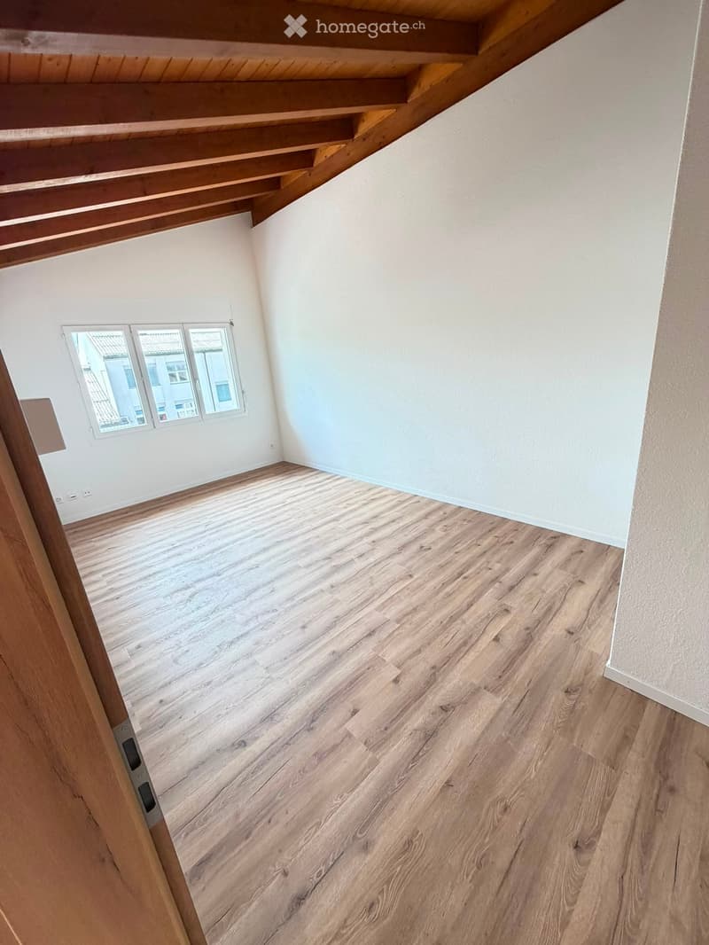 Empty room with light wooden flooring, white walls, and a window with multiple panes allowing natural light to enter.