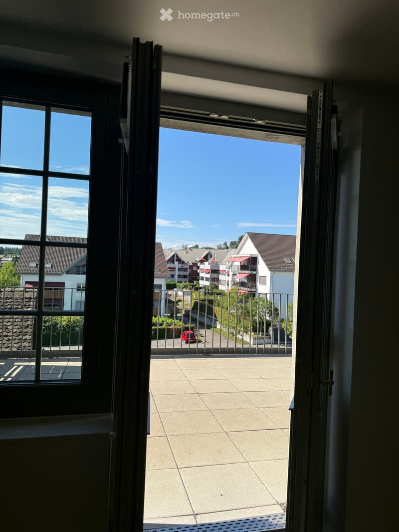 Balcony with tiled floor, metal railing, and view of residential buildings and clear sky.