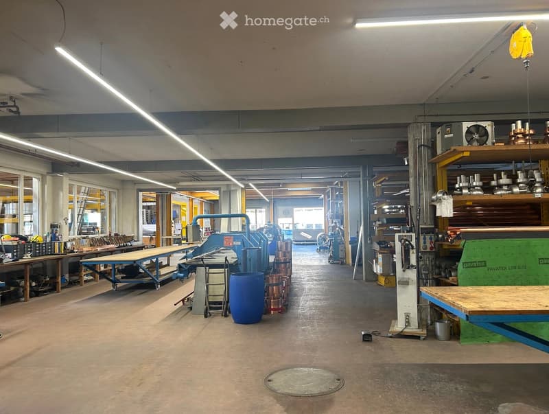 Workshop space with large windows, industrial equipment, tables, shelves, and various tools.