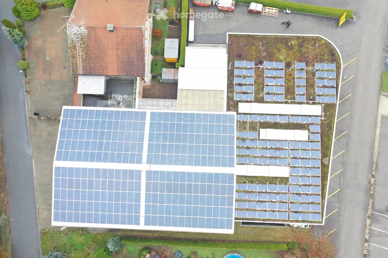 Aerial view of a building with multiple solar panels on the roof, surrounded by a parking lot and greenery.