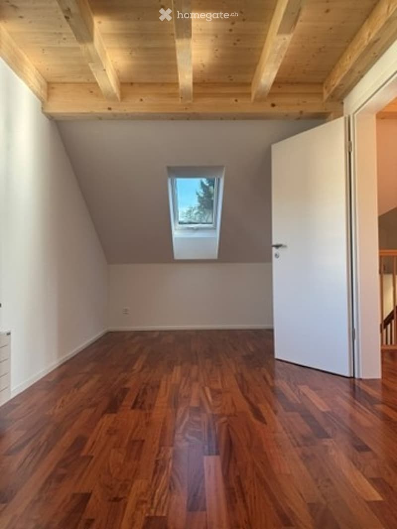 Empty attic room with wooden floor, exposed wooden ceiling beams, and a skylight window. No furniture or equipment present.