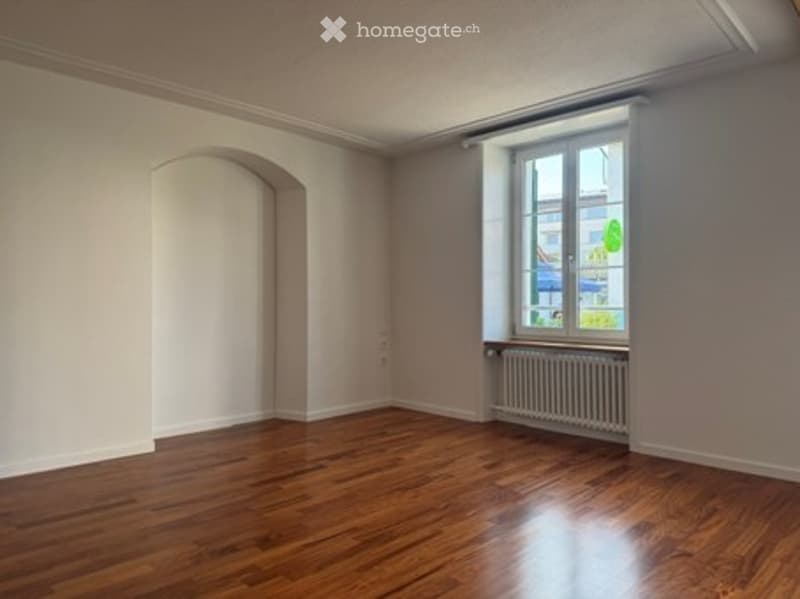 Empty room with wooden flooring, white walls, and a single window with a radiator below it. No furniture or personal items present.