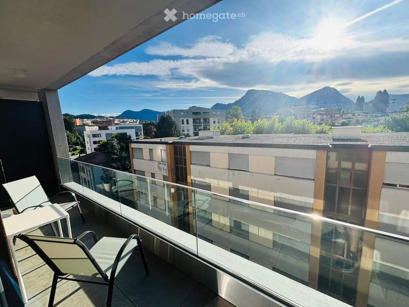 Balcony with glass railing, offering a scenic mountain view, equipped with a table and chairs.