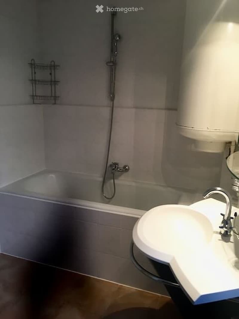 Modern bathroom with a bathtub, sink, and wall-mounted shelf. Features a glass shower enclosure and a sleek faucet design.