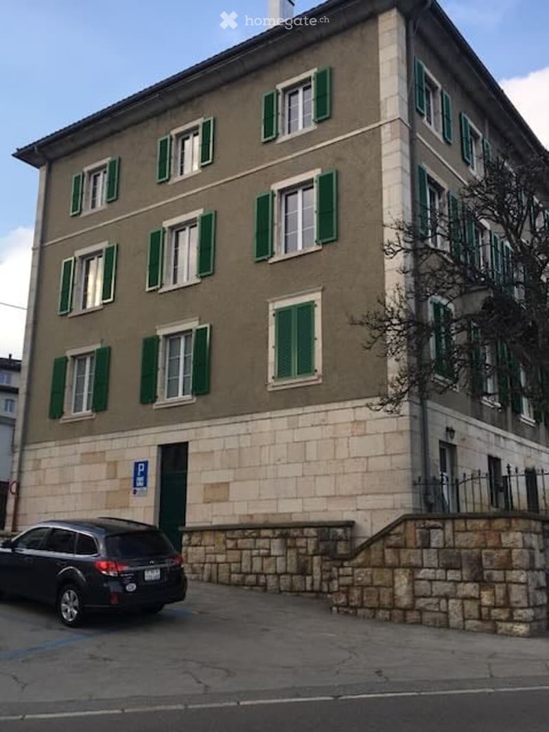 Four-story building with green shutters and stone base, parked car in front.