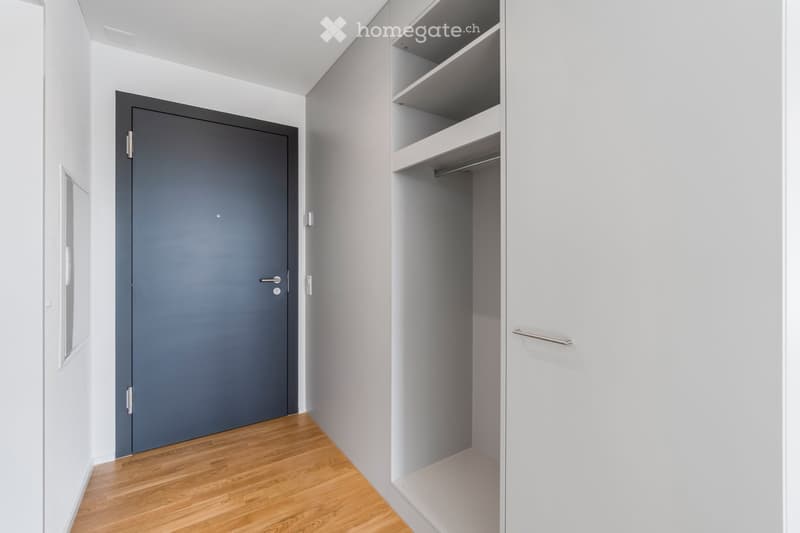 Empty room with light grey walls, wooden floor, and a built-in closet with empty shelves and a hanging rod.
