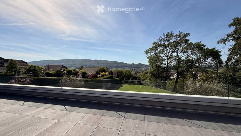 Modern balcony with a glass railing, tiled floor, and scenic view of a green landscape and distant hills.