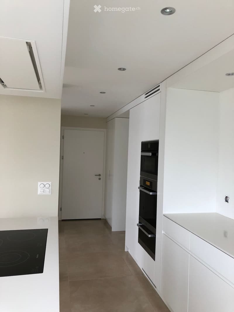 Modern kitchen with white cabinets, an induction stove, and a built-in oven. The space features recessed lighting and a neutral color palette.