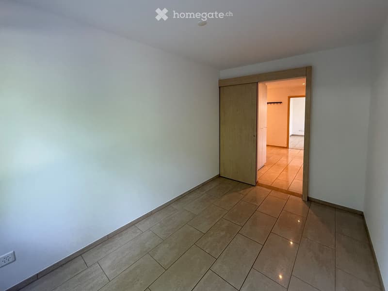 Empty room with tiled floor and white walls, featuring a wooden sliding door leading to another room.