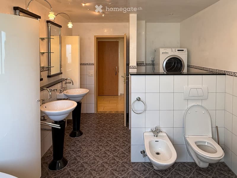 Modern bathroom with two sinks, toilet, bidet, mirror, and a washing machine on a countertop.