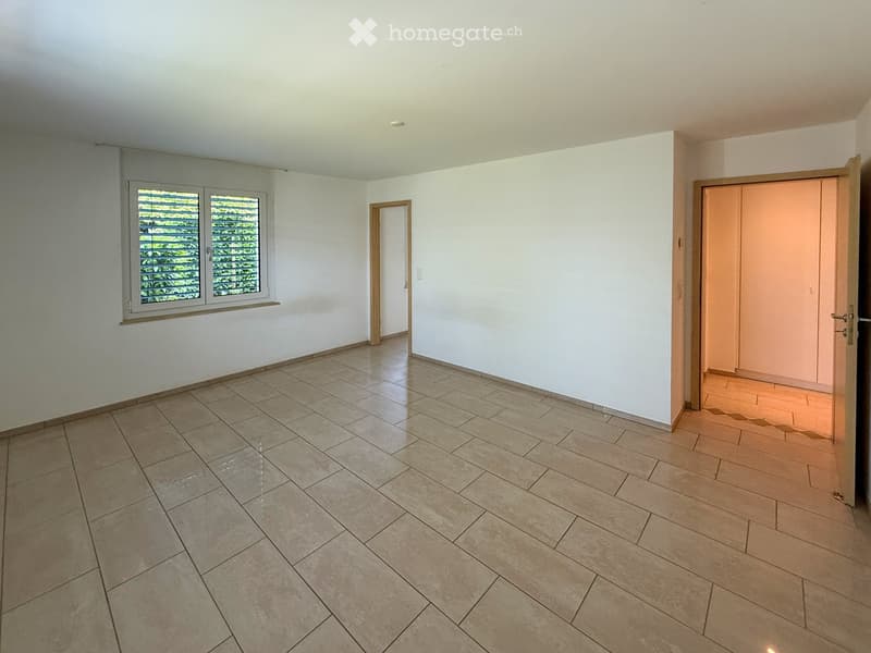 Empty room with tiled floor, white walls, and large windows with blinds. Two doors lead to adjacent spaces.