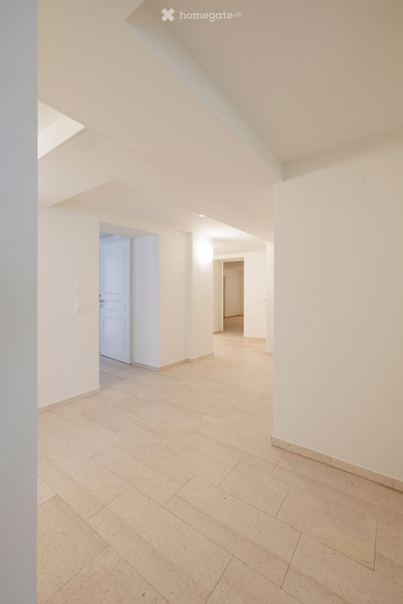 Empty hallway with light-colored tiled flooring and white walls, featuring a closed door and an open doorway leading to another room.