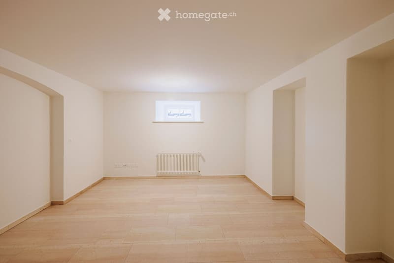 Empty room with beige tiled floor, white walls, radiator, and a small window with a decorative design.