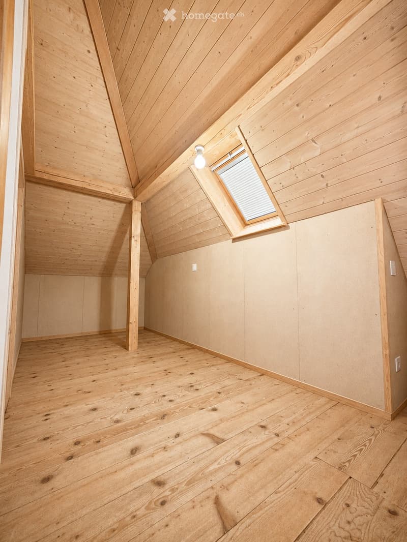 Empty room with wooden walls, ceiling, and floor, featuring a skylight window and exposed wooden beams.