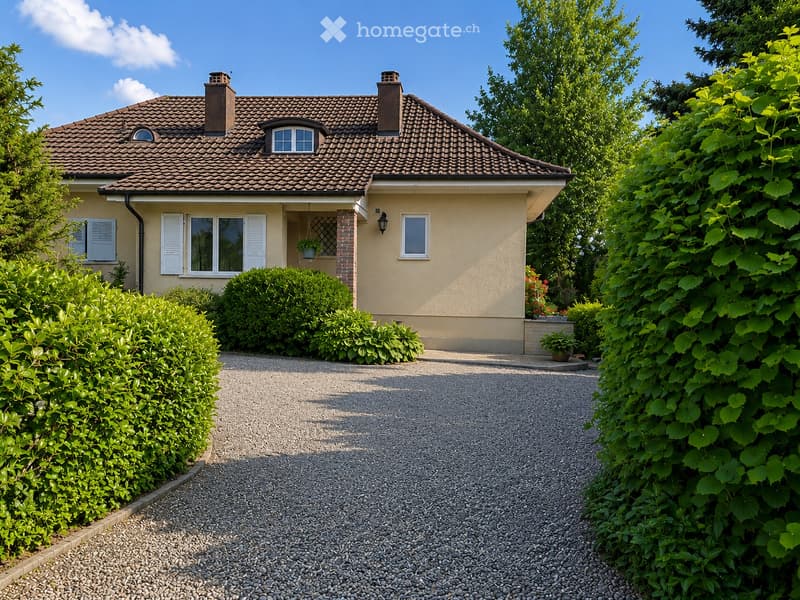 Two-story house with a tiled roof, beige exterior, white shutters, and a gravel driveway surrounded by greenery.