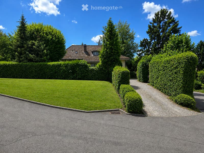 Well-maintained garden with a neatly trimmed lawn, a gravel pathway, and trimmed hedges leading to a house with a tiled roof.