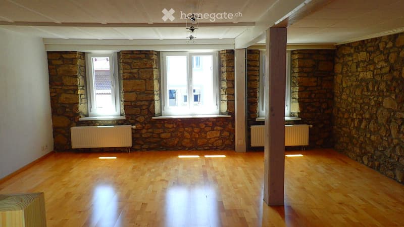 Empty room with wooden flooring, stone walls, and large windows. No furniture or equipment present.