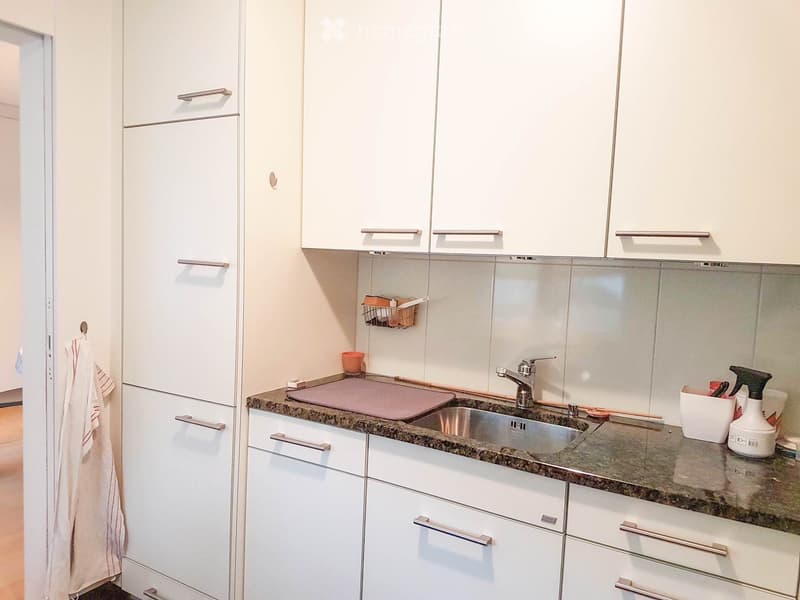 modern kitchen with white cabinets, granite countertop, stainless steel sink, faucet, chopping board, and cleaning products