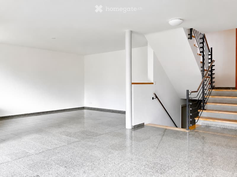 Empty room with grey tiled floor, white walls, and a staircase leading upwards with wooden steps and metal railings.