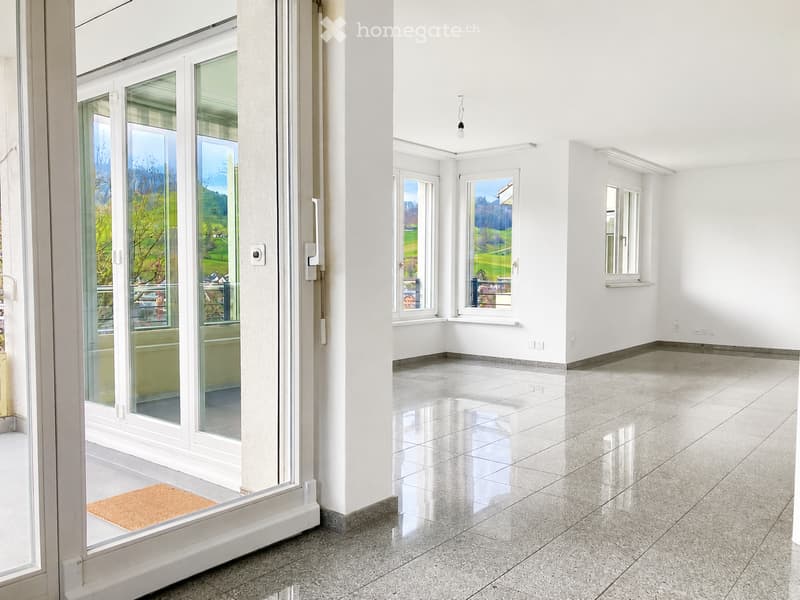 Empty room with white walls, polished tile floor, large windows, and a glass door leading to a balcony with scenic views.