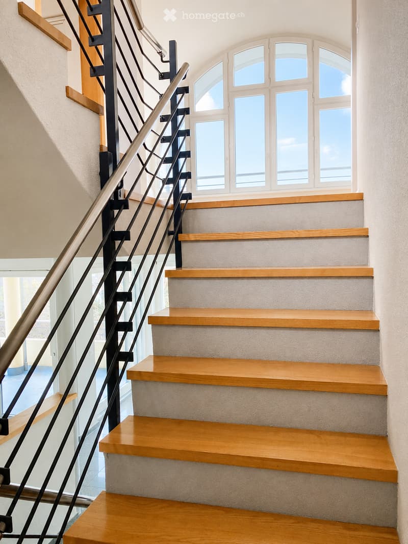 Staircase with wooden steps and a modern metal railing, leading up to a large arched window with multiple panes.