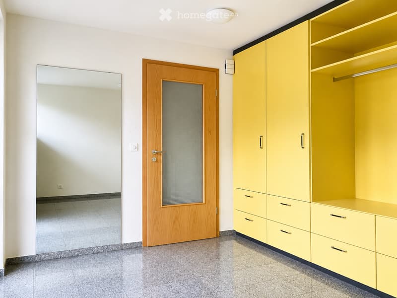 Empty room with light yellow built-in wardrobes, a wooden door, and a large mirror on the wall.