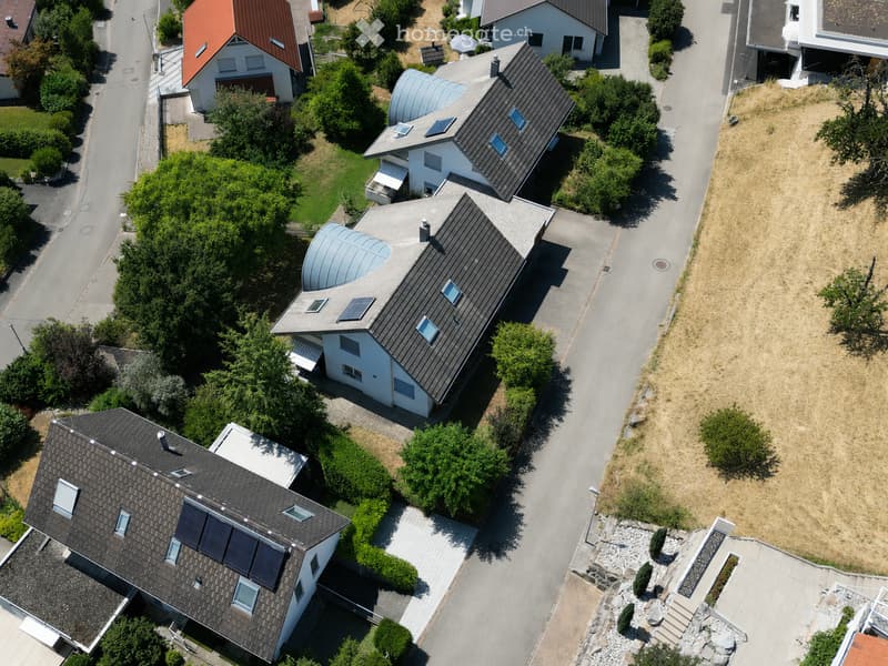 Aerial view of a residential neighborhood with multiple houses, featuring modern architecture, solar panels on roofs, and well-maintained gardens.