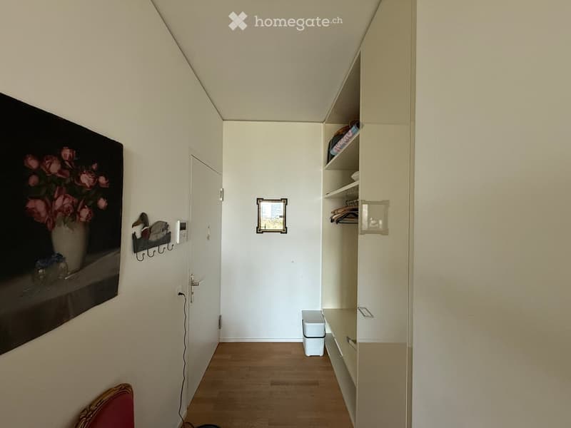 A narrow hallway with wooden flooring, white walls, built-in closet with shelves, a small trash bin, and a framed picture on the wall.