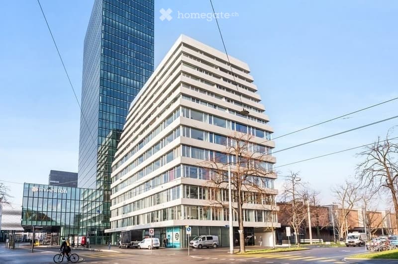 Modern multi-story building with large windows and a contemporary design, located in an urban setting with surrounding traffic and pedestrians.