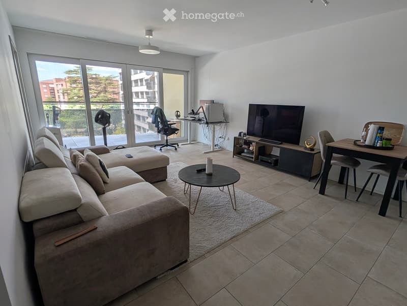 Modern living room with a beige sectional sofa, coffee table, TV, desk with chair, and a balcony view.